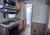 Compact RV kitchen with microwave, stovetop, sink, and fridge under wood cabinets.