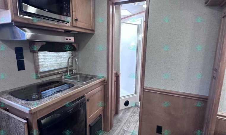 Compact RV kitchen with microwave, stovetop, sink, and fridge under wood cabinets.