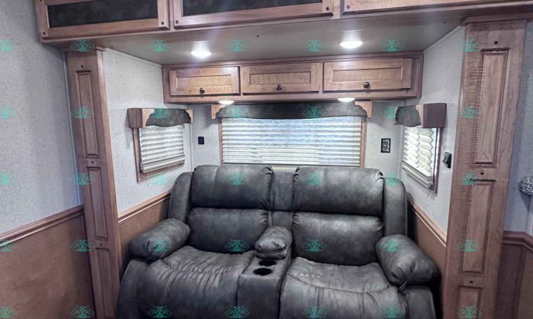 Interior of an RV living area with a dark leather sofa, wood overhead cabinets, and windows with blinds.