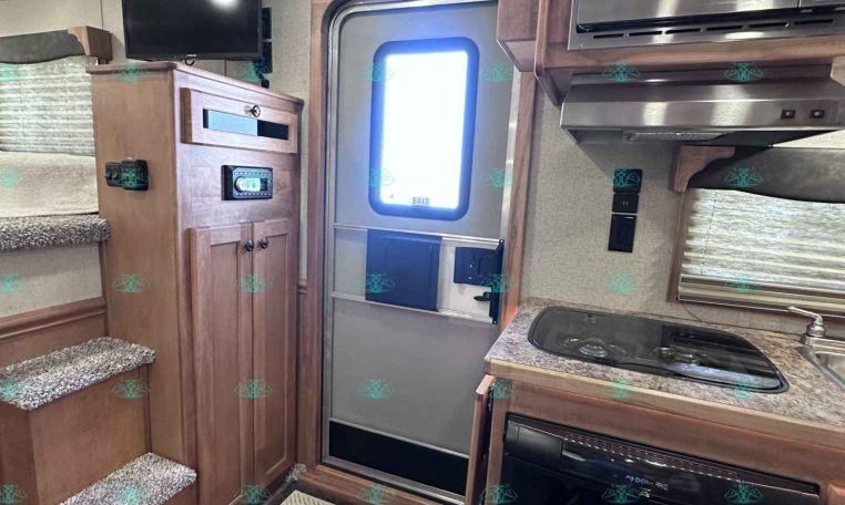 Compact RV interior showing a kitchenette with stove, fridge, and microwave, wood cabinets, and a doorway to the outside on the right.—stair steps on the left and a small TV mounted above the cabinet