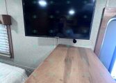 Flat-screen TV mounted on a wall above a wooden cabinet in a cozy trailer interior.