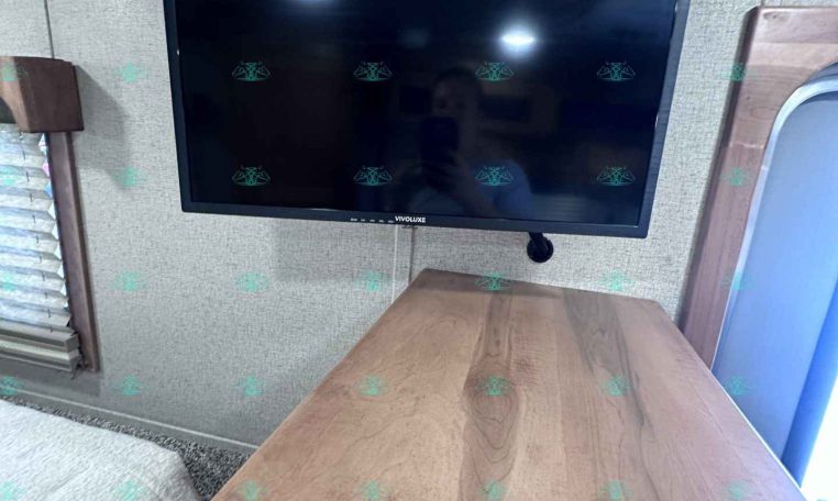 Flat-screen TV mounted on a wall above a wooden cabinet in a cozy trailer interior.