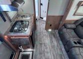 Compact RV kitchen with a two-burner stove, stainless sink, microwave above, and granite-like countertops; doorway to a small bathroom visible in the background.