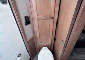 Compact RV bathroom with a white toilet flanked by wood cabinets and a panel door to the right.