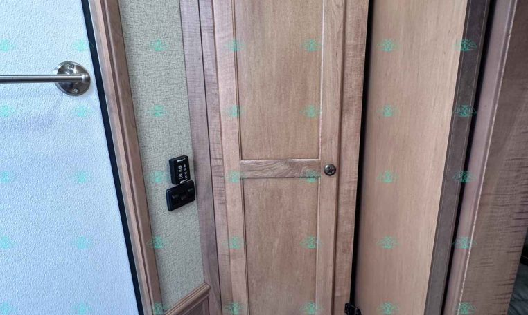Small RV bathroom with a white toilet and tall wooden cabinet, adjacent panel and door in a wood-tone interior.