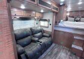 Cozy RV living area with a gray leather reclining sofa and built-in wood cabinets above in a compact space.