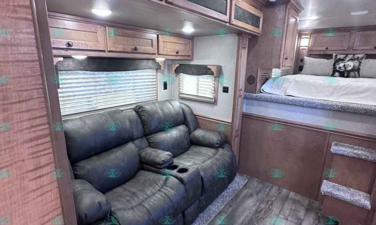 Cozy RV living area with a gray leather reclining sofa and built-in wood cabinets above in a compact space.