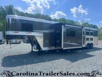 Large gray-and-white fifth-wheel trailer with an extended slide-out parked on a gravel lot, blue sky and trees in the background.