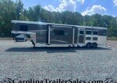 Long dark gray fifth-wheel trailer with a slide-out, parked on a gravel lot with a treeline in the background.