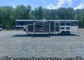 Long gray Merhow horse trailer parked on a gravel lot with green trees and a blue sky in the background.