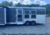Merhow horse trailer with three axles, dark gray exterior, and side stalls with barred windows, parked on gravel with trees in the background.