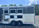 Merhow horse trailer: dark gray body with three side windows, chrome trim, and dual-axle wheels on gravel under a blue sky.