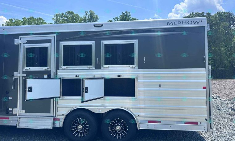 Merhow horse trailer: dark gray body with three side windows, chrome trim, and dual-axle wheels on gravel under a blue sky.