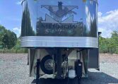 Metal horse trailer with Merhow Stampede logo in front, parked on gravel under a blue sky