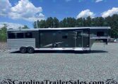 Side view of a dark gray Merhow horse trailer with two axles, parked on a gravel lot with trees in the background.