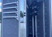 Open trailer showing a vertical auger conveyor inside, likely for grain handling or bulk material transfer.