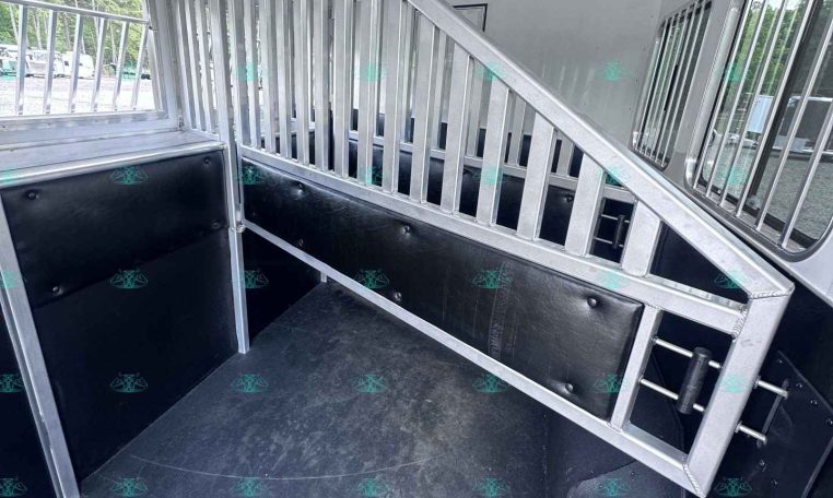 Interior of a aluminum horse trailer with a partition and stair ramp, black padded walls, and windows along the side.