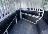 Interior of a horse trailer with aluminum divider bars, padded lower walls, and a non-slip black floor plus a small staircase ramp inside