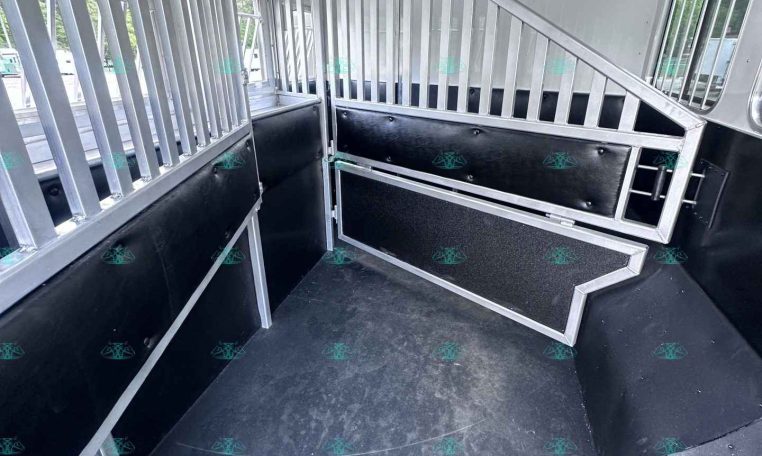 Interior of a horse trailer with aluminum divider bars, padded lower walls, and a non-slip black floor plus a small staircase ramp inside