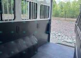 Interior of an empty aluminum horse trailer with barred windows along the side and a dark rubber floor