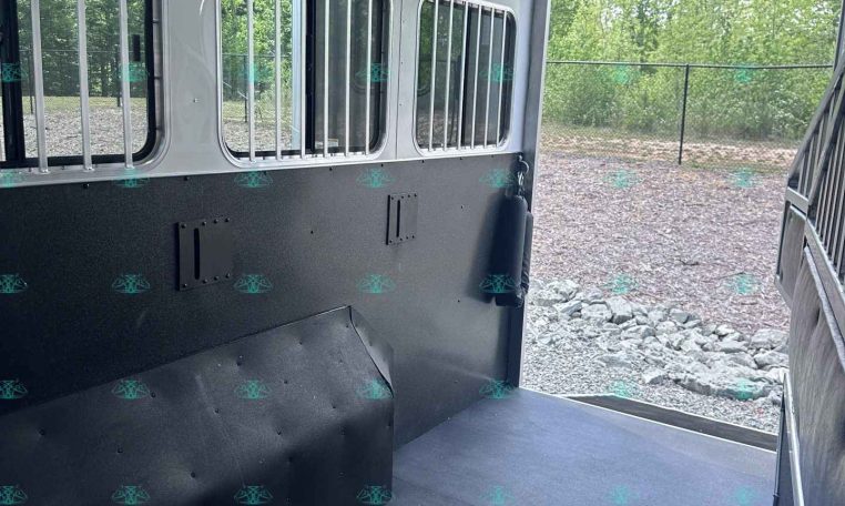 Interior of an empty aluminum horse trailer with barred windows along the side and a dark rubber floor