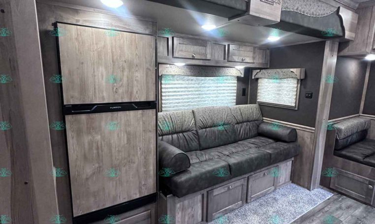 RV living area with built-in fridge, upper bunk, and gray wood cabinets along a windowed wall