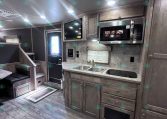 Interior view of a travel trailer's kitchen with gray wood cabinets, microwave, sink, and countertop.