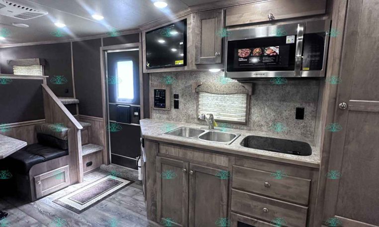 Interior view of a travel trailer's kitchen with gray wood cabinets, microwave, sink, and countertop.