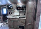 RV kitchen with gray wood cabinets, stainless microwave, double sink, and island underneath bright ceiling lights
