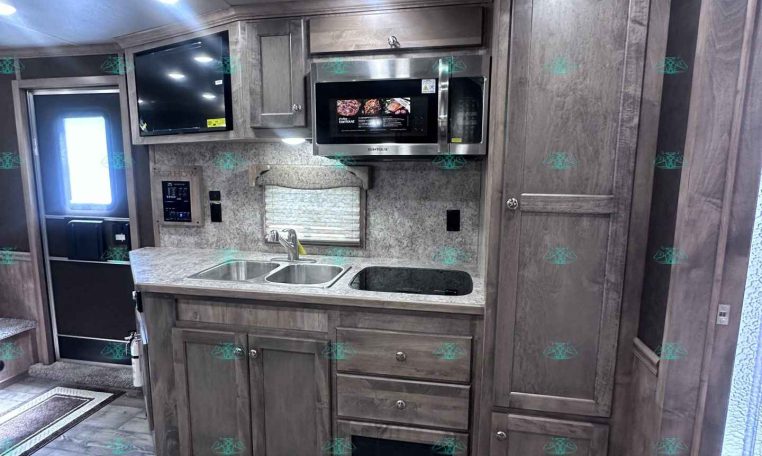 RV kitchen with gray wood cabinets, stainless microwave, double sink, and island underneath bright ceiling lights