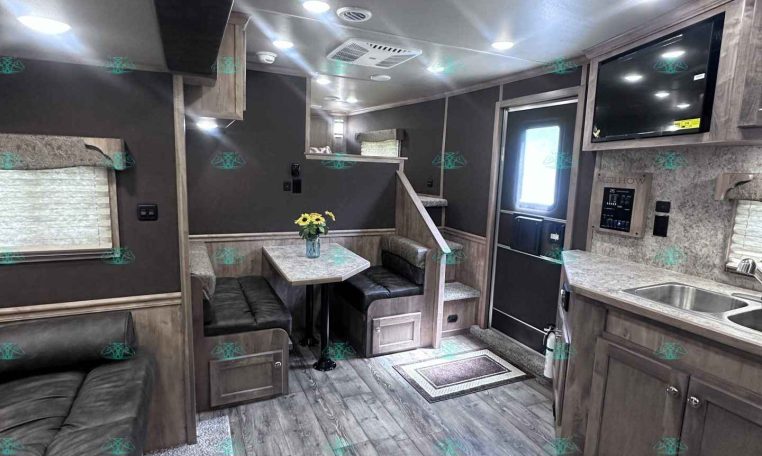 Interior of a modern RV trailer living area with dining booth, sofa, and overhead cabinets in gray wood tones.