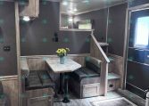 Interior of a cozy trailer dining booth with a gray wood table, cushioned bench seating, and a vase of sunflowers on the table.