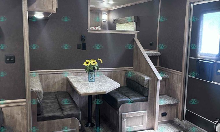 Interior of a cozy trailer dining booth with a gray wood table, cushioned bench seating, and a vase of sunflowers on the table.