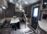Interior of a modern camper with a U-shaped booth, marble table, and a vase of sunflowers on the table.