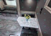 Interior of a gray-toned RV living area with a sofa, overhead cabinets, and a small table with sunflowers in a vase on the counter.