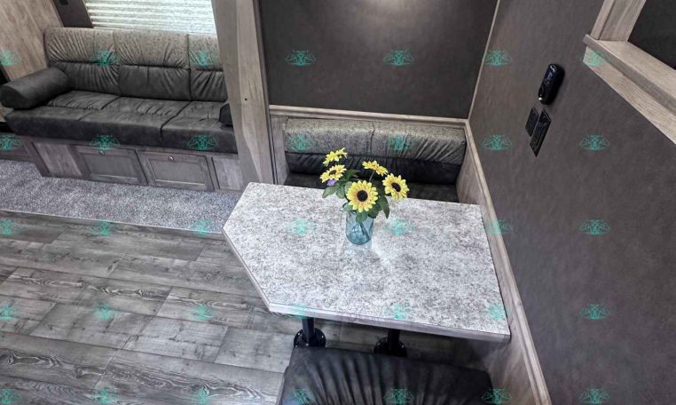 Interior of a gray-toned RV living area with a sofa, overhead cabinets, and a small table with sunflowers in a vase on the counter.