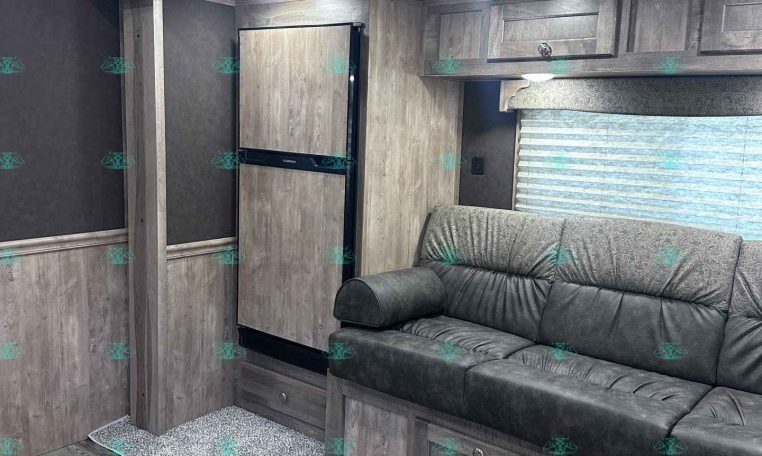 Interior of a modern RV living area with gray wood cabinets, a sofa, and a tall refrigerator beside a pillar and window blinds