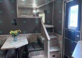 Interior of a modern travel trailer with a small dining nook, gray wood cabinetry, and a loft area above. Chief features: sunflowers on the table and a staircase leading up to the loft.