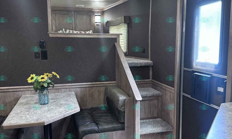 Interior of a modern travel trailer with a small dining nook, gray wood cabinetry, and a loft area above. Chief features: sunflowers on the table and a staircase leading up to the loft.