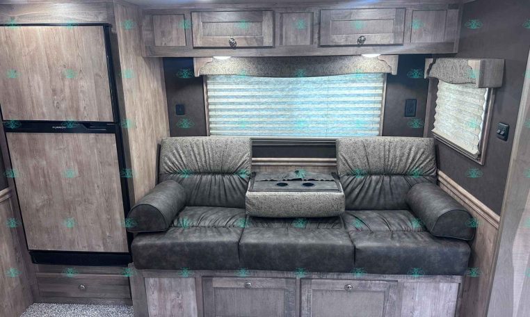 Interior of a travel trailer living area with gray wood cabinets, a gray sofa, and a large window with blinds.