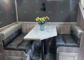 Booth-style dining area in a trailer with gray upholstered benches, a light gray speckled table, and a vase of yellow sunflowers in the center.