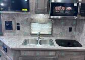 RV kitchen with grey wood cabinets, double sink, and a stainless microwave above the counter