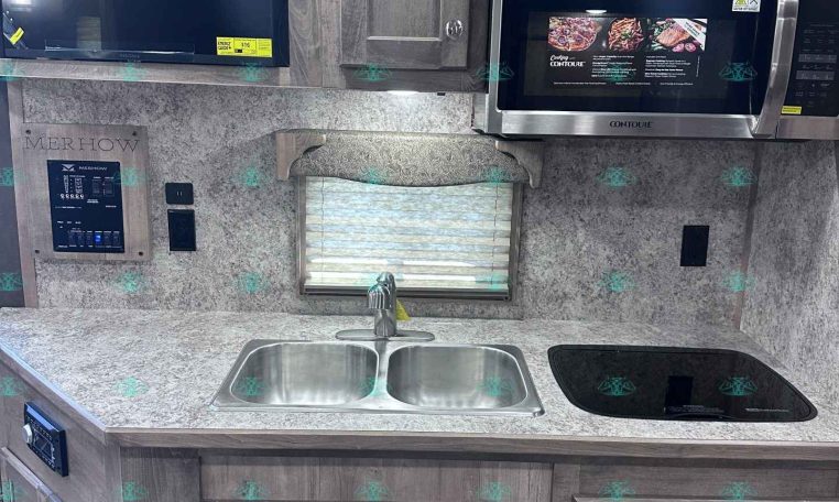 RV kitchen with grey wood cabinets, double sink, and a stainless microwave above the counter
