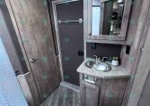 Compact camper bathroom with wood-grain cabinets, a small sink, and a mirrored medicine cabinet above.