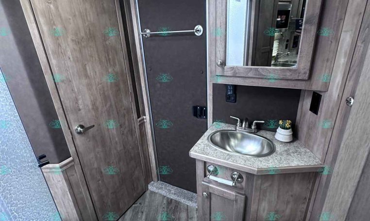 Compact camper bathroom with wood-grain cabinets, a small sink, and a mirrored medicine cabinet above.