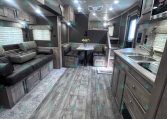 Interior of a modern RV/travel trailer with gray wood cabinets, a sofa, and a small dinette area in the center.