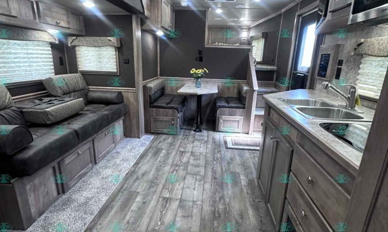 Interior of a modern RV/travel trailer with gray wood cabinets, a sofa, and a small dinette area in the center.