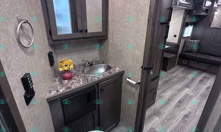 Bathroom in a trailer: vanity with granite countertop, circular sink, mirrored cabinet, towel ring, and toilet.