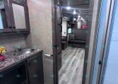 RV bathroom with dark wood cabinets, granite counter, sink, and visible toilet; door opens to living area.