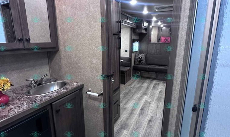 RV bathroom with dark wood cabinets, granite counter, sink, and visible toilet; door opens to living area.